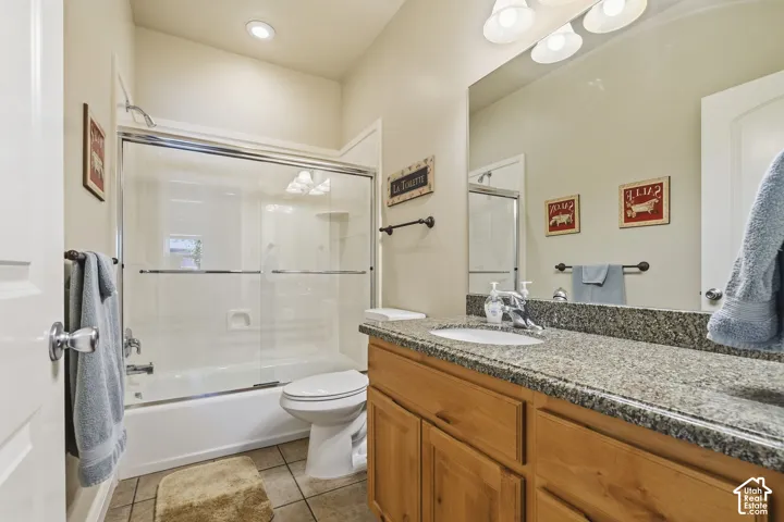 Bathtub with sliding glass enclosure, recessed lighting, double vanity light fixture, integrated sink, and wood-finish cabinetry