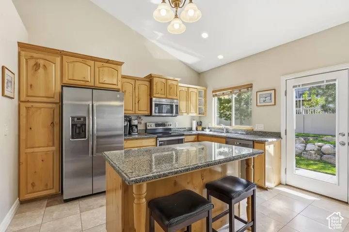 Vaulted ceiling kitchen featuring wood cabinetry, stainless steel appliances, granite countertops, and tile flooring