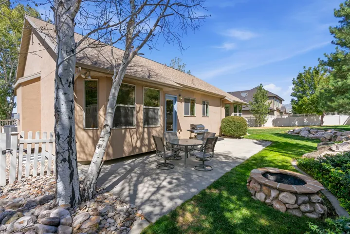 Expansive outdoor patio with a built-in stone fire pit, mature landscaping, a manicured lawn, and a light-toned stucco exterior
