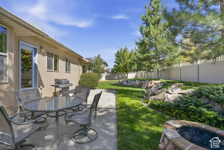 Expansive backyard featuring a concrete patio, a built-in stone-finish fire pit, mature trees, a rock feature with integrated plantings, and a privacy fence