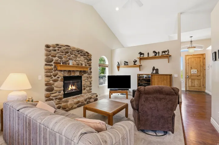 Vaulted ceiling, stone-clad fireplace with mantel, arched window, wood-finish flooring, paneled entry door