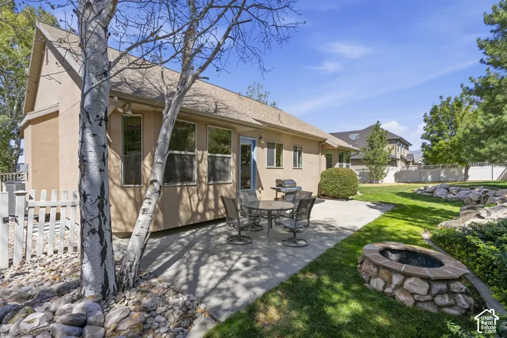 Expansive outdoor patio with a built-in stone fire pit, mature landscaping, a manicured lawn, and a light-toned stucco exterior