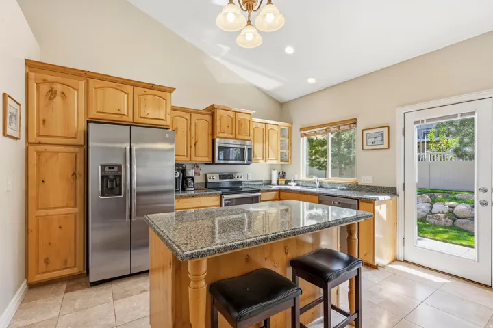 Vaulted ceiling kitchen featuring wood cabinetry, stainless steel appliances, granite countertops, and tile flooring