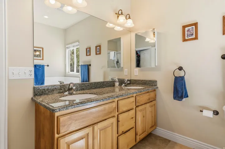 Dual vanity with light wood cabinetry, granite countertop, and undermount sinks