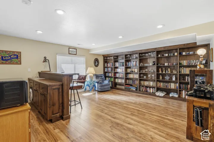 Built-in wood-finish shelving, recessed ceiling lighting, wood-finish flooring, built-in wet bar with wood-finish cabinetry, and a window with horizontal blinds