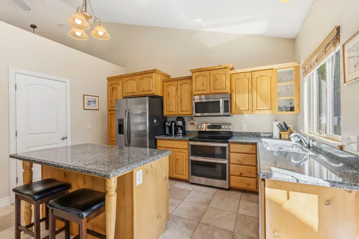 Kitchen featuring a vaulted ceiling, wood cabinetry, stainless steel appliances, granite countertops, and tile flooring