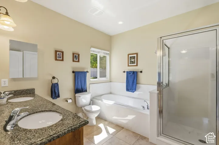 Dual vanity with undermount sinks and granite-finish countertop, built-in soaking tub, separate glass-enclosed shower, and tiled flooring