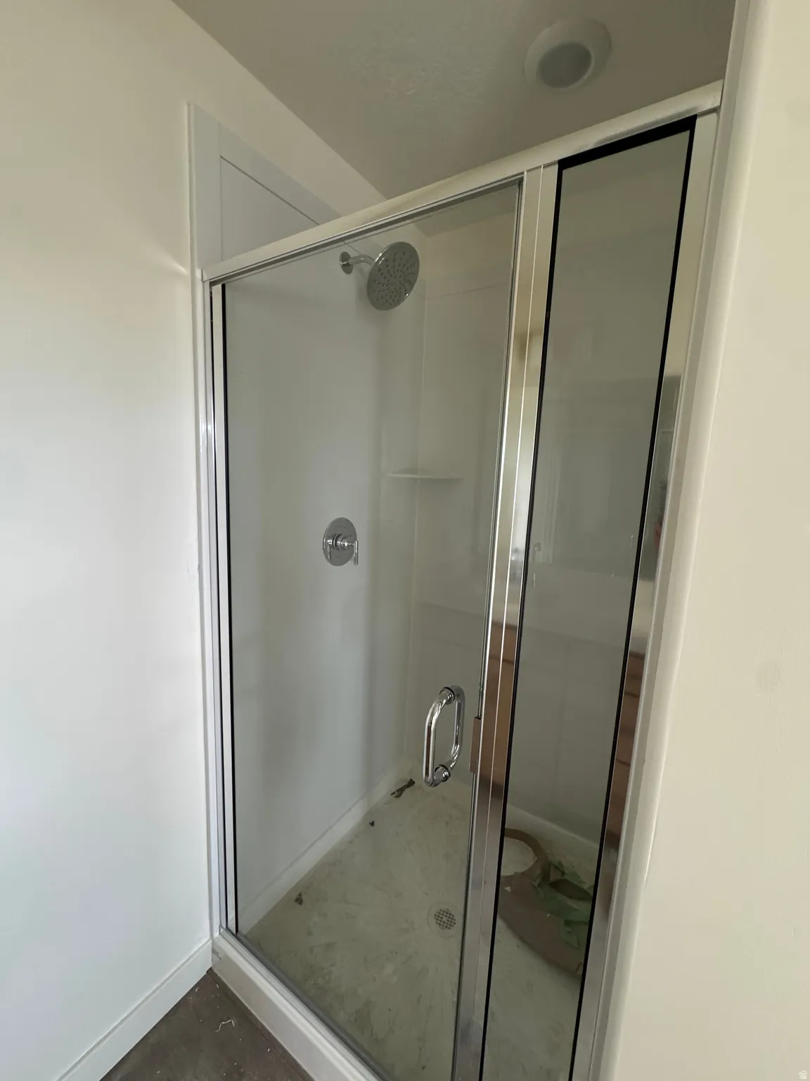 Glass-enclosed shower with a chrome rainfall showerhead and integrated shelving