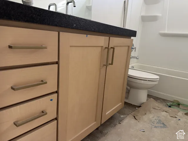 Light wood-finish vanity with drawer and cabinet storage, featuring a dark countertop and chrome fixtures