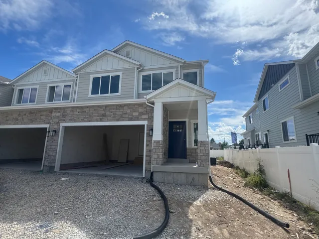 Stone facade accenting, multi-pane windows, covered entry porch, dark-finish entry door, attached garage bays