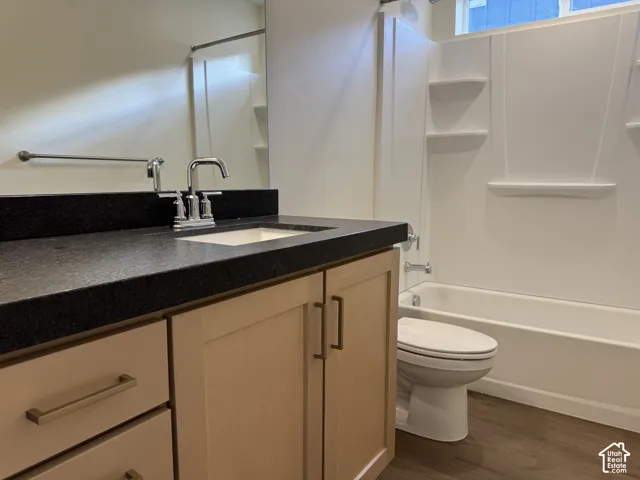 Bathroom featuring a light-toned wood vanity with dark stone countertop, undermount sink, tub and shower combination with integrated shelving, and wood-finish flooring