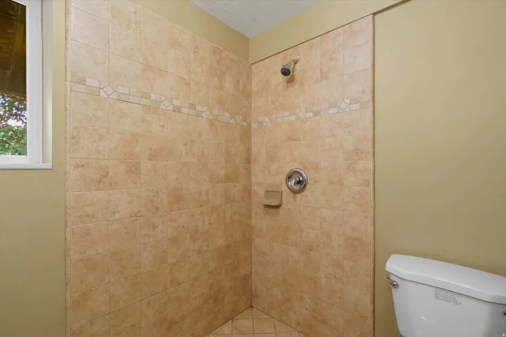 Tiled shower enclosure featuring a decorative accent band, corner shelf, and chrome fixtures