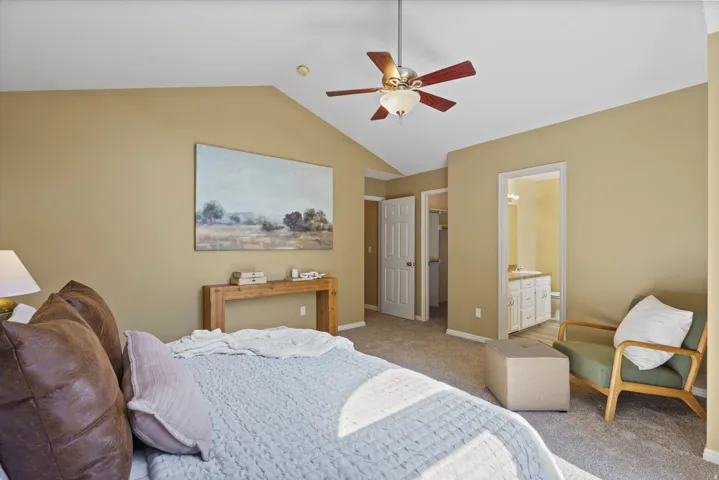 Vaulted ceiling with an attached ceiling fan, neutral carpet flooring, and an en-suite bathroom with a vanity and built-in cabinetry