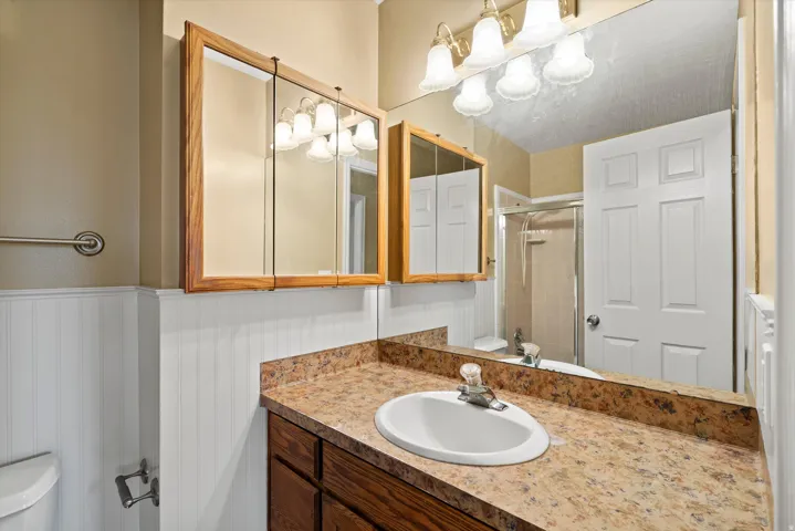 Bathroom featuring a single vanity with an integrated sink, a built-in medicine cabinet, a full-width wall mirror, and wainscoting