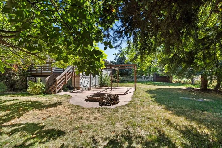 Expansive backyard with a wooden deck, concrete patio, fire pit, and wooden pergola frame