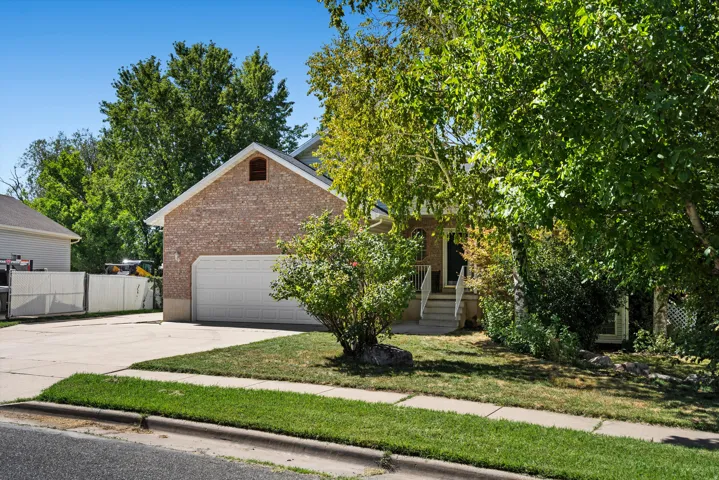 Brick exterior with a gable roofline, attached garage, concrete driveway, and established landscaping