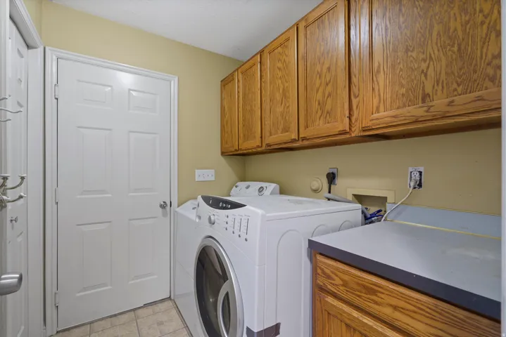 Laundry area featuring wood-finish cabinetry, a neutral countertop, and tiled flooring