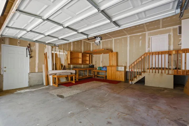 Concrete flooring with an interior door, paneled garage door, and wood stairs with railing