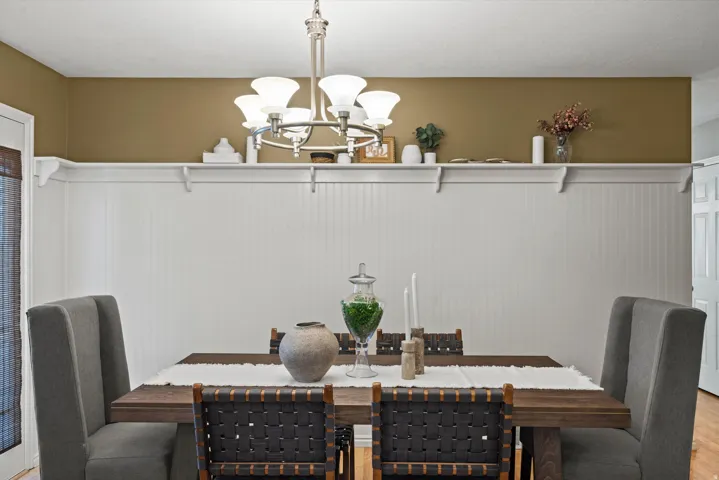 Wood-finish dining table with upholstered and woven chairs, board and batten wall detailing, and a built-in display shelf