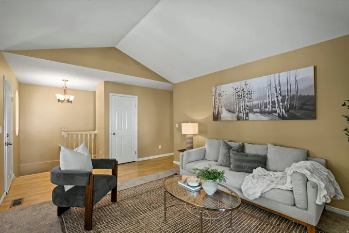 Vaulted ceiling design, neutral wall tones, wood-finish flooring, and a classic chandelier fixture