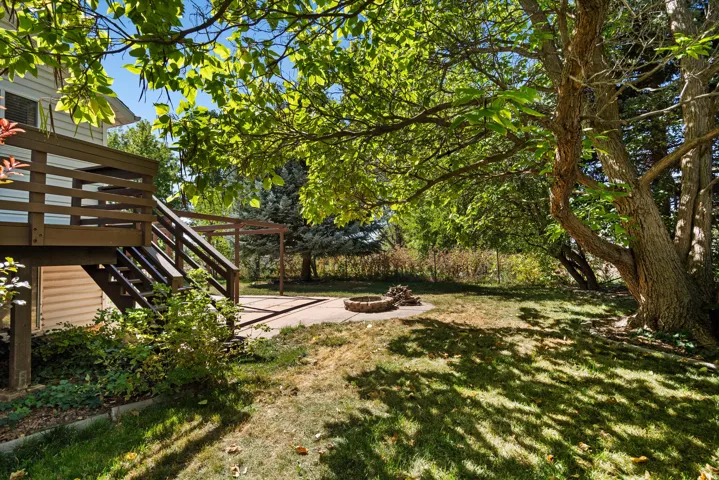 Spacious backyard with a multi-level wood deck, ground-level paver patio, integrated fire pit, and mature trees providing natural shading