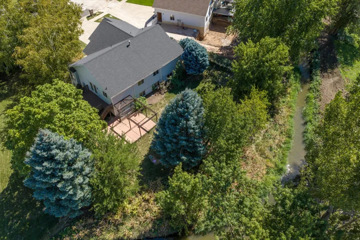 Expansive outdoor living area featuring a multi-level deck, mature trees, and natural waterway along the property line