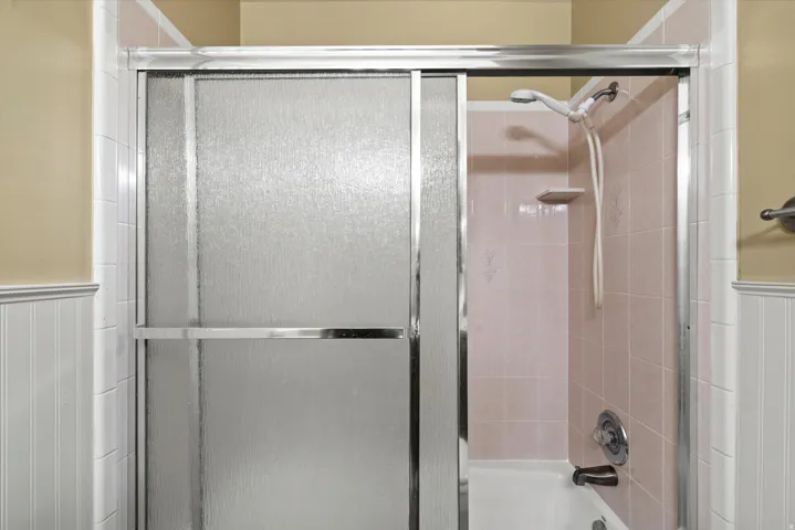 Bathtub with tile surround, shower fixture, and sliding glass enclosure