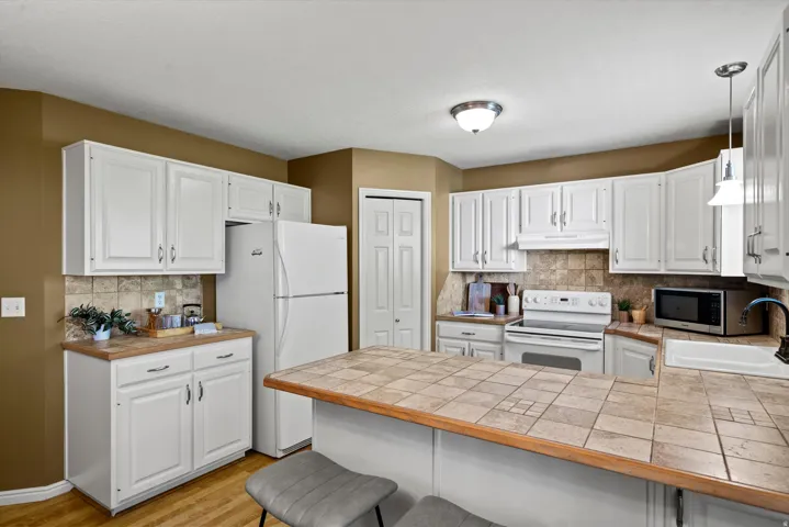 White cabinetry, tile backsplash, tile countertop island, stainless steel sink, and wood-finish flooring
