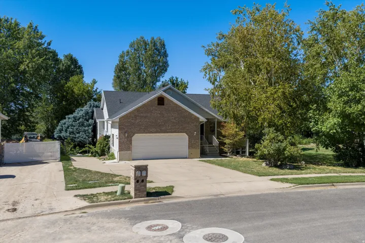 Brick and siding exterior with a dark shingle roof, attached two-car garage, concrete driveway, and mature landscaping