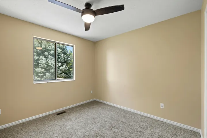 Wall-to-wall carpeting, neutral wall finishes, a window with exterior tree scenery, a ceiling fan with integrated lighting, and white trim