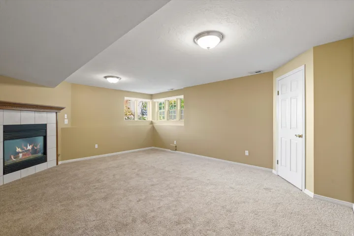 Recessed ceiling with flush mount lighting, bay window, tile-surround fireplace with wood mantel, panel door, and neutral-tone carpeting