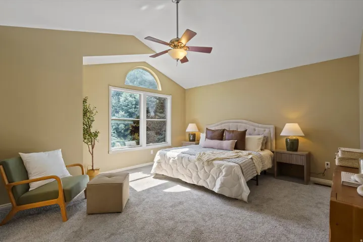 Vaulted ceiling with ceiling fan, large window with arched transom, and carpeted flooring