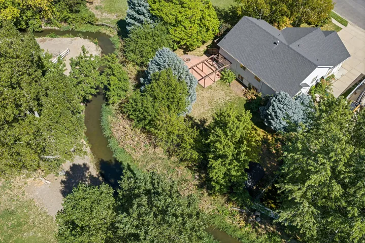 Expansive property featuring a winding creek, mature trees, a multi-level deck, and a distinct roofline