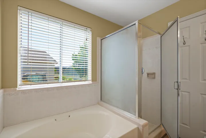 Built-in soaking tub with a tiled surround, adjacent shower enclosure with frosted glass panels, and a window featuring horizontal blinds