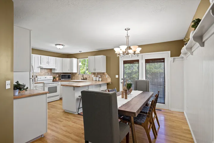 Kitchen and dining area featuring wood-finish flooring, white cabinetry, integrated appliances, and a dining space with double glass-paneled doors