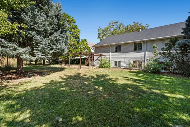 Expansive outdoor space featuring a paved patio, a wood pergola, mature trees, and a substantial lawn area