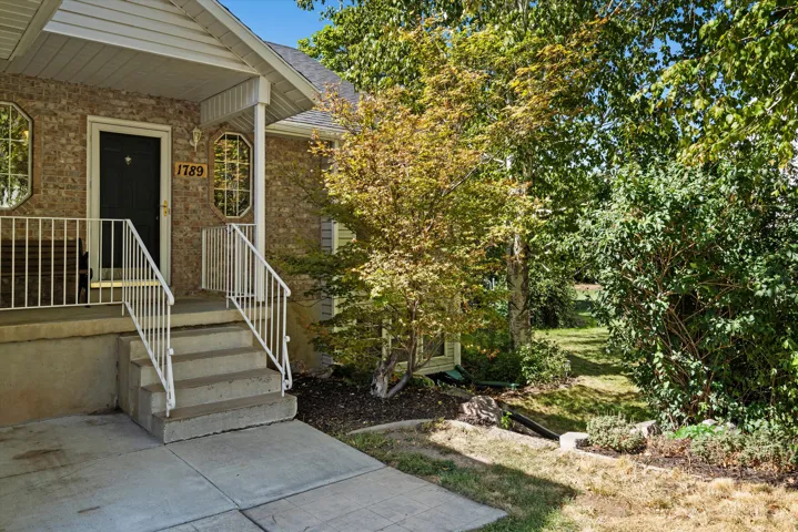Brick exterior with concrete porch, white railings, and mature landscaping