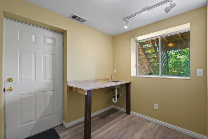 Light wood-finish flooring, built-in sink with countertop, track lighting, and a sliding window