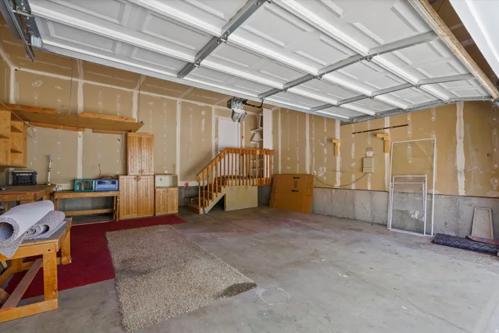 Spacious garage featuring a concrete floor, overhead garage door, built-in wooden cabinetry, and an interior staircase with wood railing
