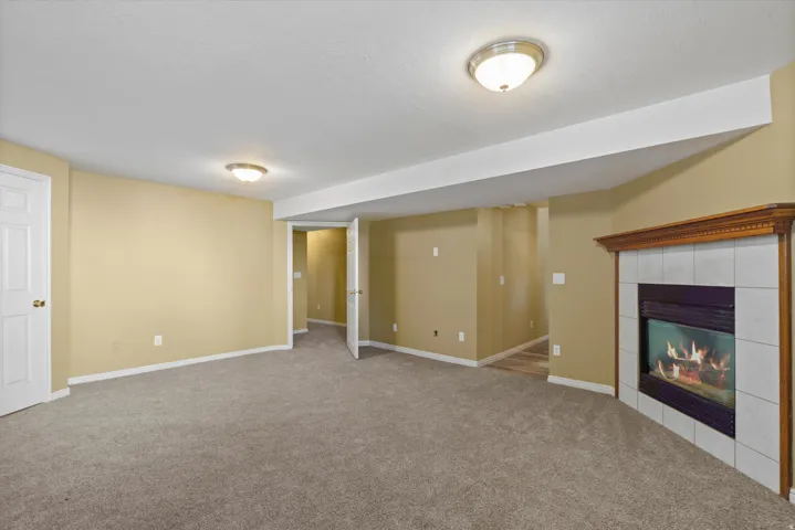 Spacious room featuring neutral carpeting, recessed lighting, and a fireplace with a wood-finish mantel and tile surround