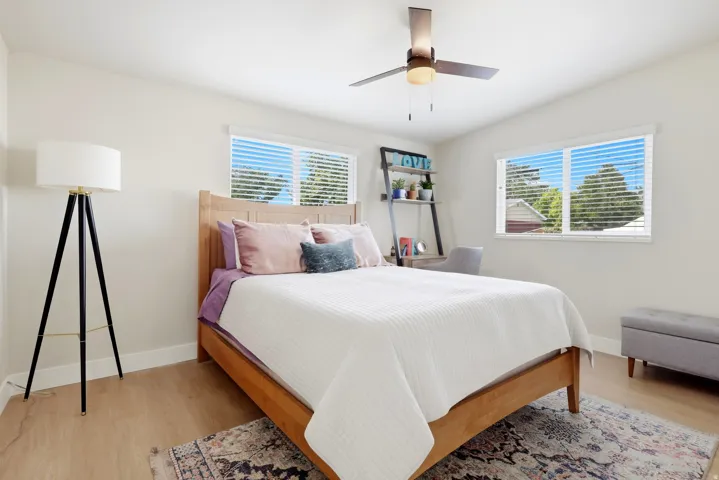 Light-toned walls, two windows with blinds, wood-finish flooring, and a ceiling fan with integrated lighting