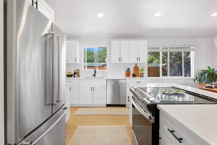 Contemporary kitchen featuring stainless steel appliances, white cabinetry, integrated sink, and wood-finish flooring
