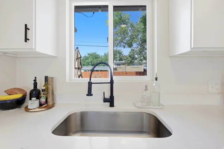 White cabinetry with matte black hardware, stainless steel undermount sink, black gooseneck faucet, and light-toned countertop
