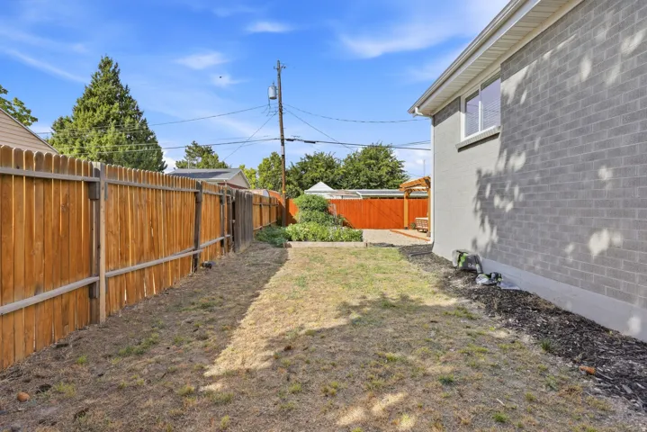 Wood-panel fencing enclosing a grassy yard, featuring a grey brick exterior and a window with white trim