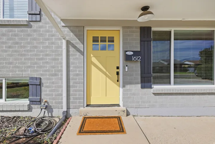 Light gray brick exterior with a bright yellow front door featuring divided lites