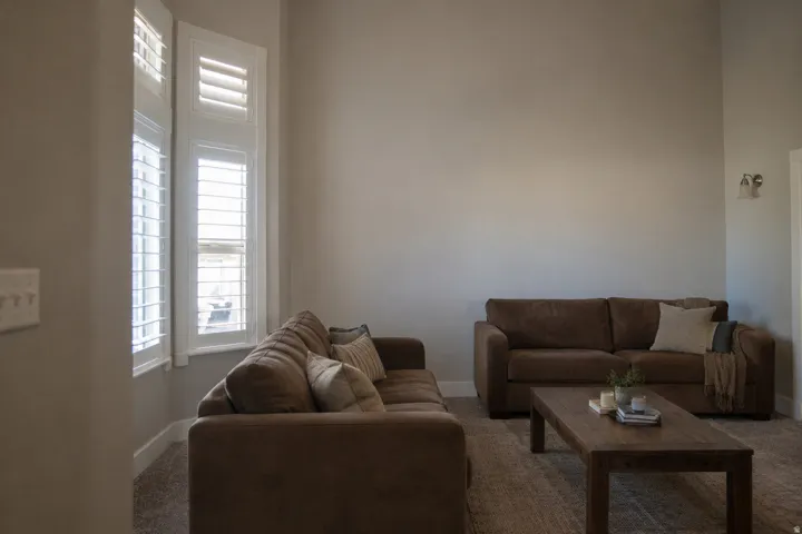 Bay window with plantation shutters and white trim, wall-mounted sconce lighting, and carpeted flooring