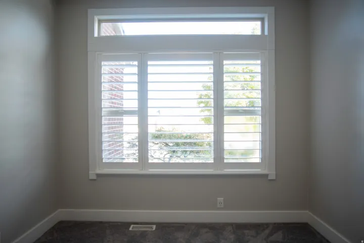 Window featuring white plantation shutters and transom, neutral wall color, and dark carpet