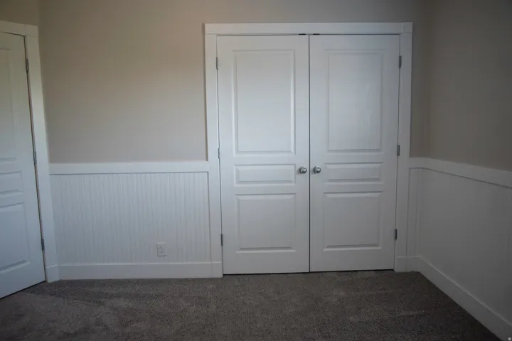 White paneled bi-fold doors, white beadboard wainscoting, and neutral wall paint