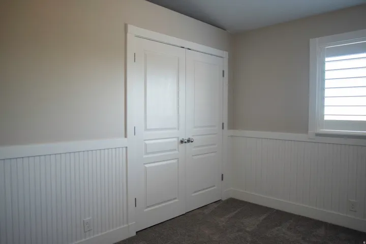 Paneled bifold closet doors, wainscoting, and carpeted flooring