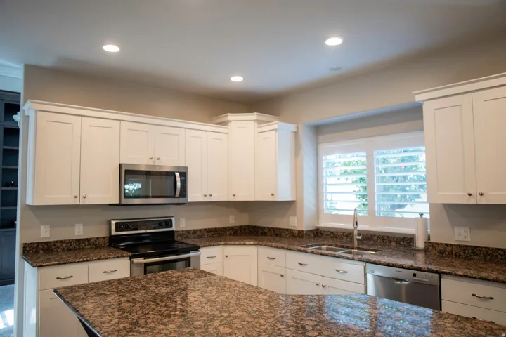 White shaker-style cabinetry with crown molding, stainless steel appliances, speckled stone countertops, undermount sink, and recessed lighting